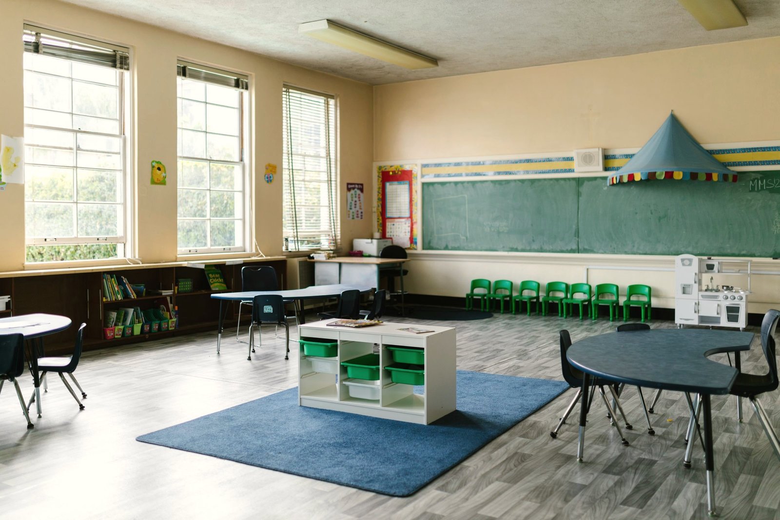 A preschool classroom with a blue rug, low shelves and child sized tables.