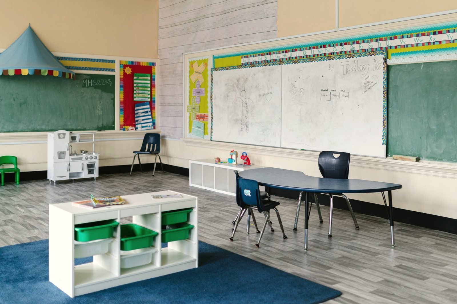 A preschool room with chalkboards, a play kitchen and a low table with chairs.