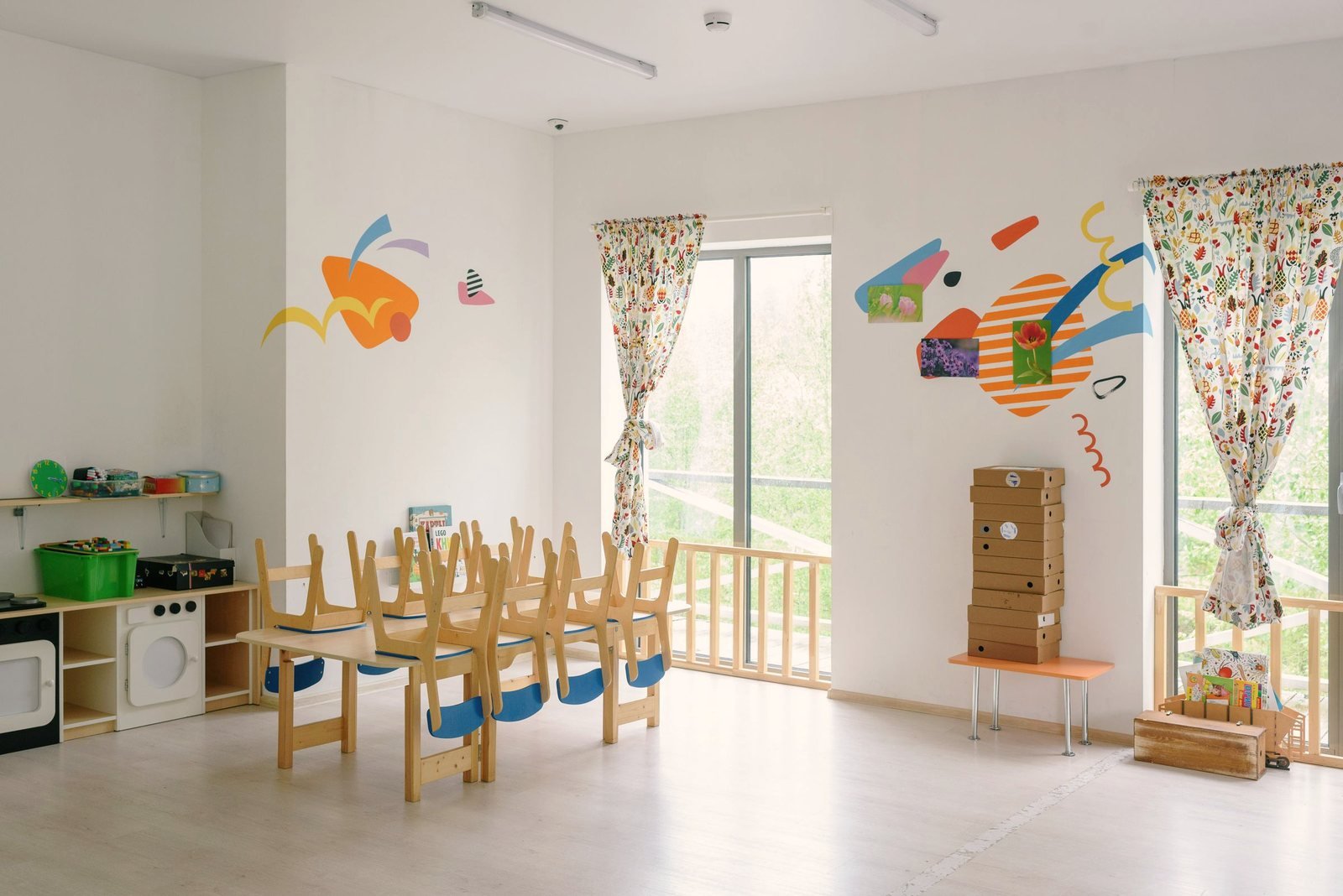 Child sized chairs stacked at a table in a bright classroom with tall windows.