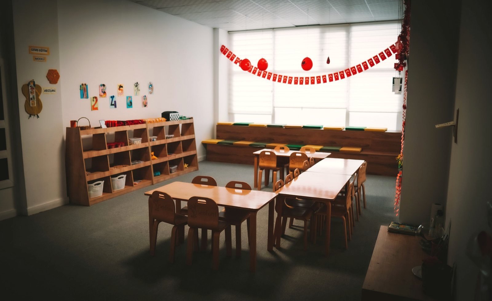 A wall of wooden cubbies with baskets beside low tables in a preschool room.