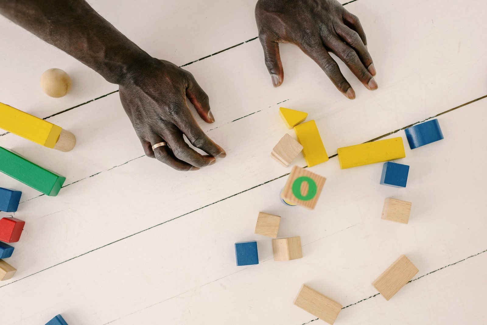 Adult hands sorting coloured wooden blocks and letter cubes on a white floor.