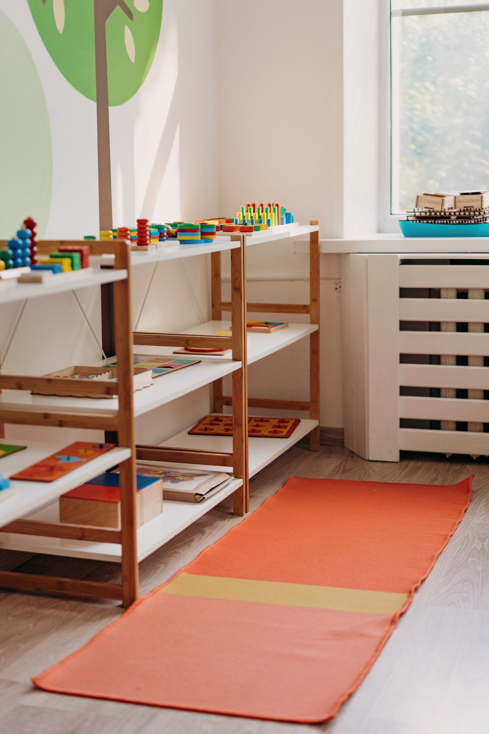 Low open shelves holding sorting toys, puzzles and stacking rings by a window.