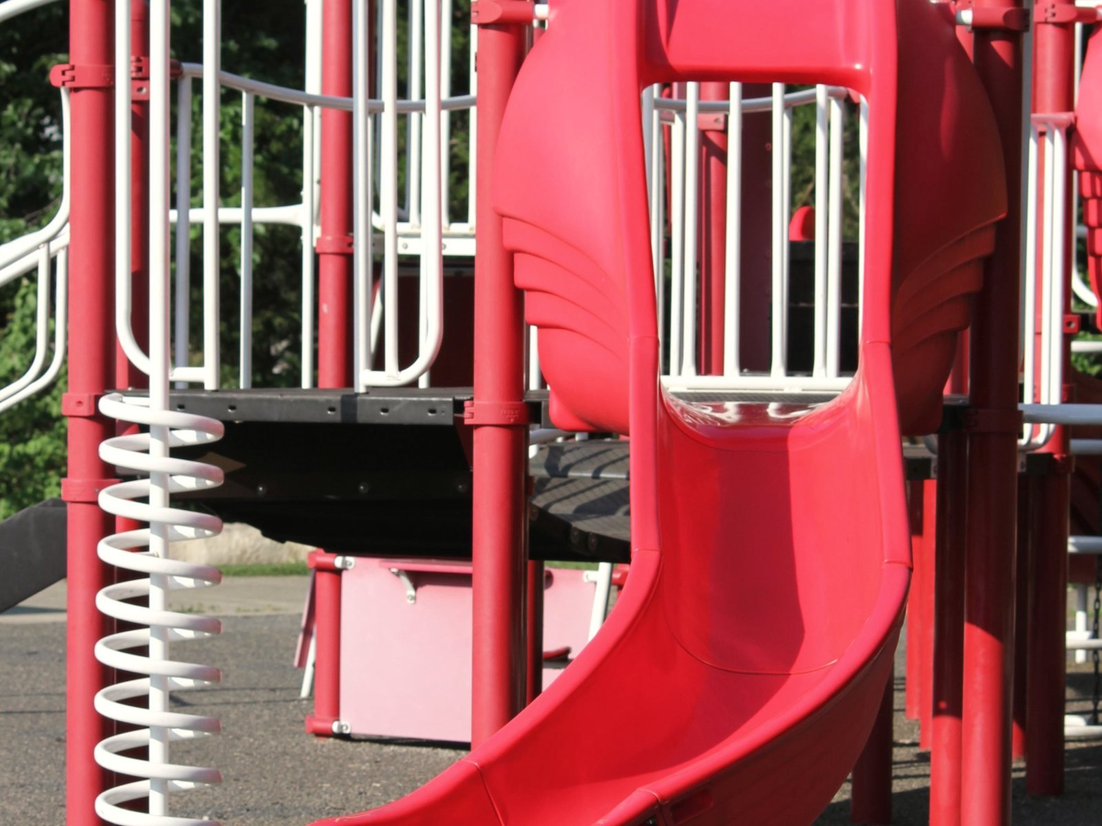 An outdoor playground slide and climbing structure over safety surfacing.